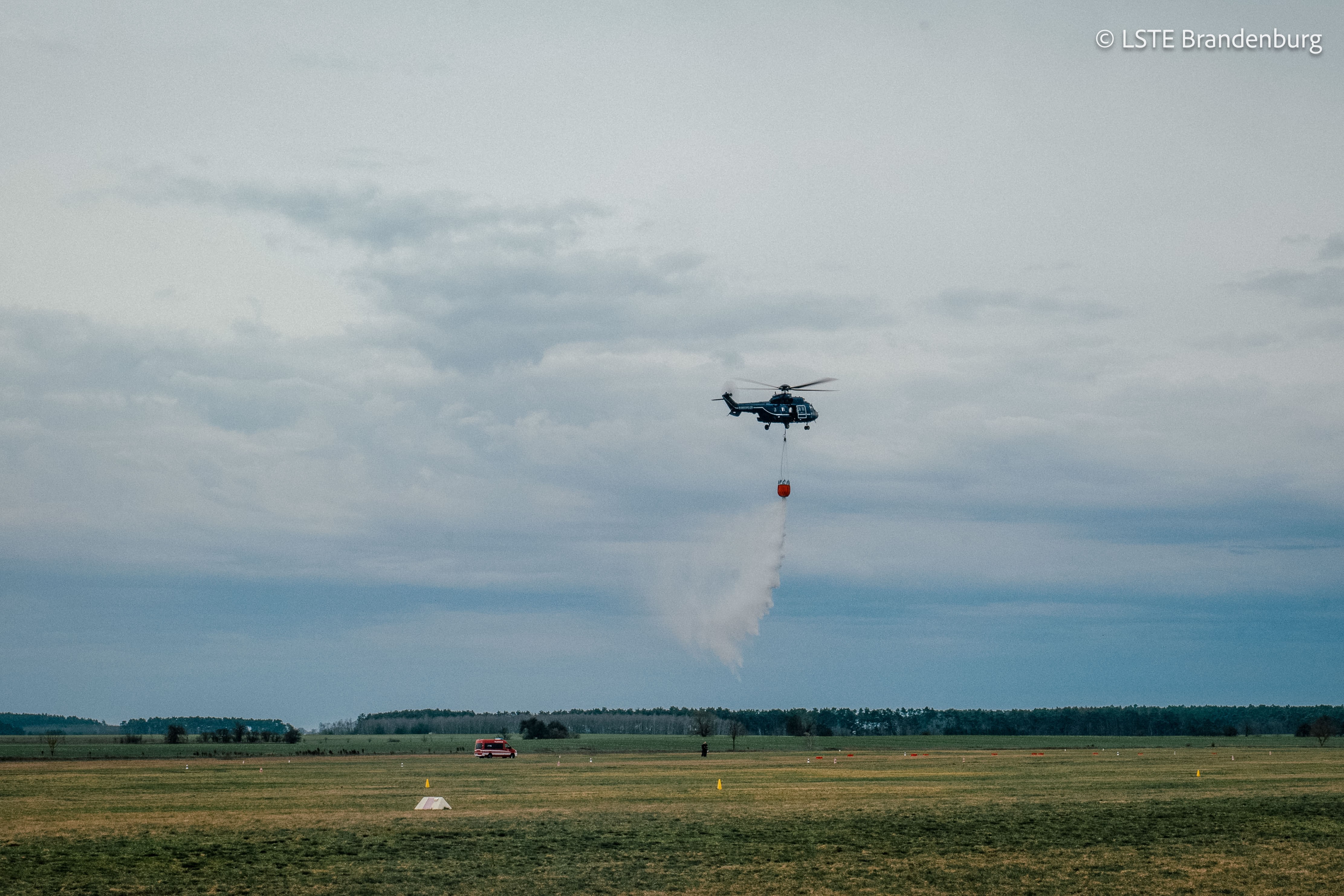 Ein Hubschrauber der Bundespolizei wirft Löschwasser auf einer Freifläche ab