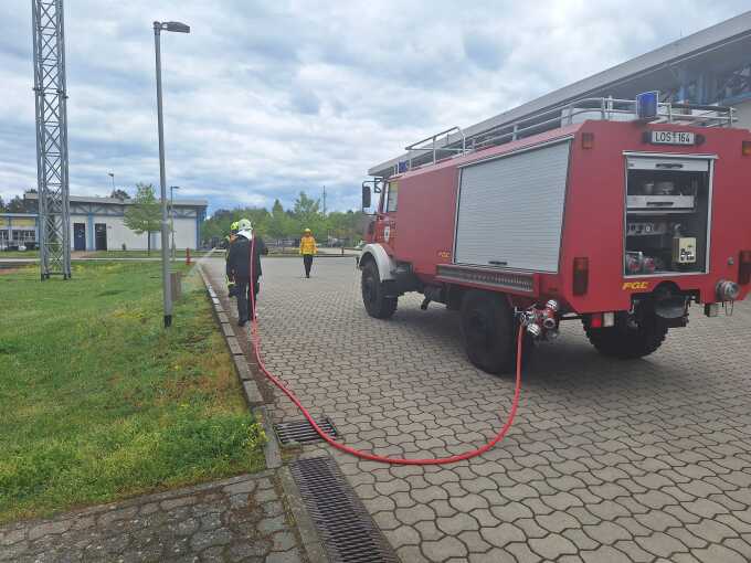 Feuerwehrangehörige laufen neben einem langsam fahrenden Tanklöschfahrzeug und löschen den Bereich neben sich ab